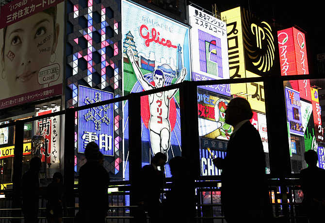 Passers-by are silhouetted against advertisements in the Dotonbori shopping and amusement district in Osaka.