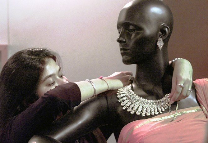 An attendent decorates a mannequinn with silver jewellery.