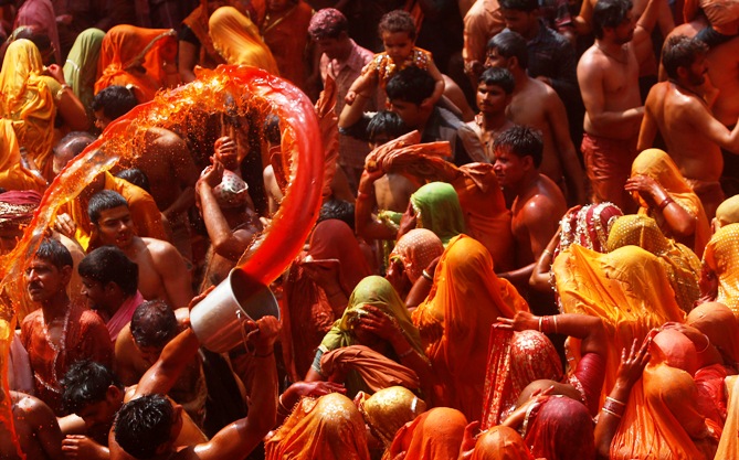A man flings a pail of orange coloured water towards a group of women during Huranga at the Dauji temple near Mathura.