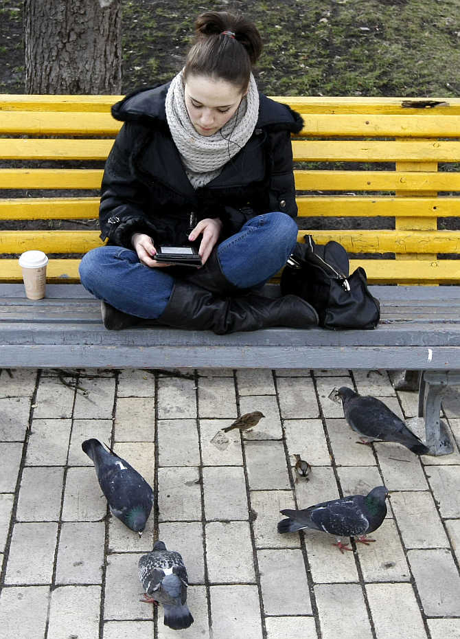 A woman sits on a bench and looks at her tablet in a park in Kiev, Ukraine.