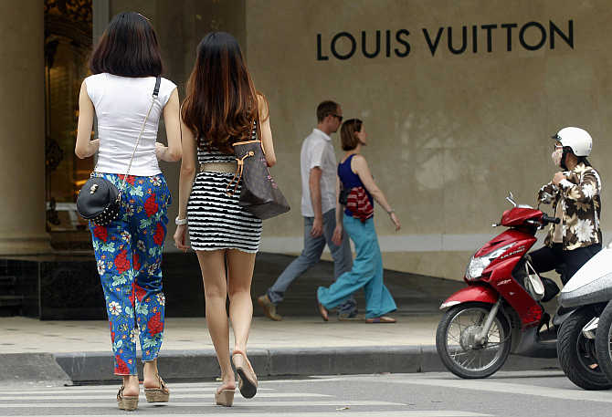 Women walk next to a Louis Vuitton sign as they enter the luxury Trang Tien Plaza shopping mall in Hanoi, Vietnam. The community is also present in Vietnam.