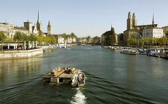 A worker steers a boat and a pontoon on the Limmat River during sunny spring weather in Zurich.
