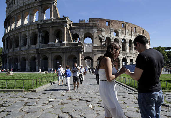 Tourists use an iPad tablet in front of Rome's ancient Colosseum, Italy.