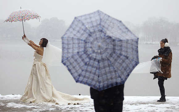 A woman wearing a wedding dress poses for pictures in snow next to the West Lake of Hangzhou, Zhejiang province.