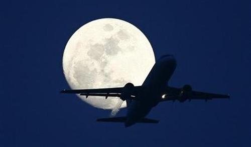 A passenger aircraft is silhouetted against the rising moon.