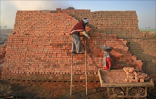 A village woman holds her child while carrying clay on her head as she works at a road construction site under National Rural Employment Guarantee Act.