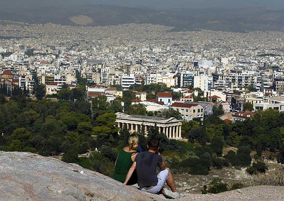 Tourists sit on a hill overlooking Athens outside the archaeological site of the Acropolis.