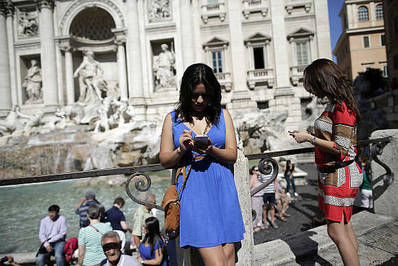 Women use smartphones in front of the Trevi Fountain in Rome, Italy.