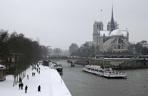 A tourist boat travels along the River Seine near the snow-covered Notre Dame Cathedral in Paris.