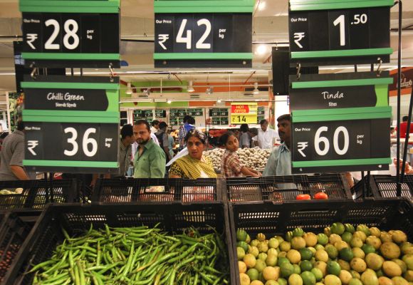 Prices for various vegetables are displayed as people shop in the fresh foods section of a supermarket.