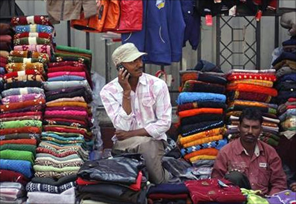 A vendor speaks on his mobile phone as he waits for customers at his roadside shop selling clothes in Mumbai.