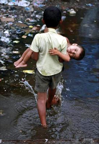 Ashfaq carries his two-year-old brother Farhaan through a flooded pathway in a Mumbai slum.