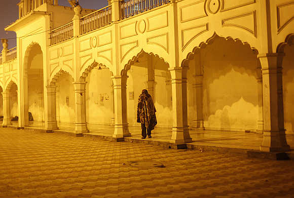 A homeless man wrapped in a blanket walks inside a Sikh temple compound on a cold winter night in New Delhi.