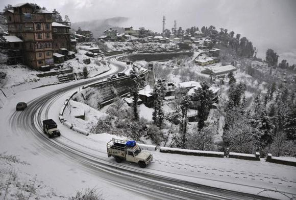 Vehicles drive down a snow-covered road after heavy snowfall in Shimla. 
