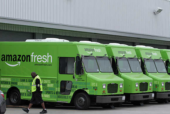 A worker walks past Amazon Fresh delivery vans parked at an Amazon Fresh warehouse in Inglewood, California.