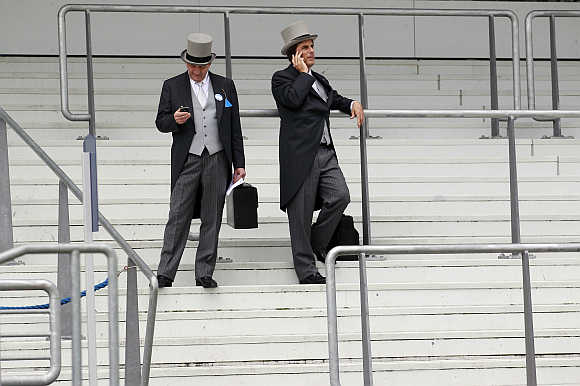 Two racegoers talk on their mobile phones on the fourth day of racing at Royal Ascot in southern England.