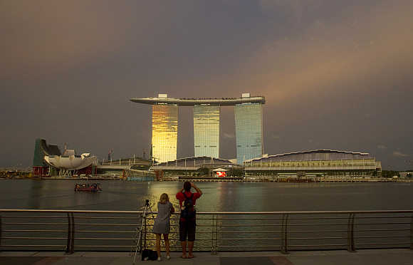 Tourists stand at a promenade across the water from the Marina Bay Sands integrated resort in Singapore.