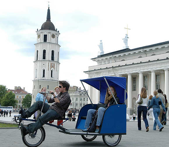 A man drives a city resident in a Velomobile outside the cathedral in Vilnius, Lithuania.