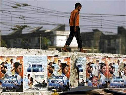 A boy living on the street walks on a wall displaying publicity posters of Golden Globe award-winning film.