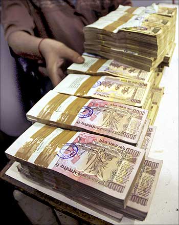 A teller arranges stacks of rupee notes in a bank.