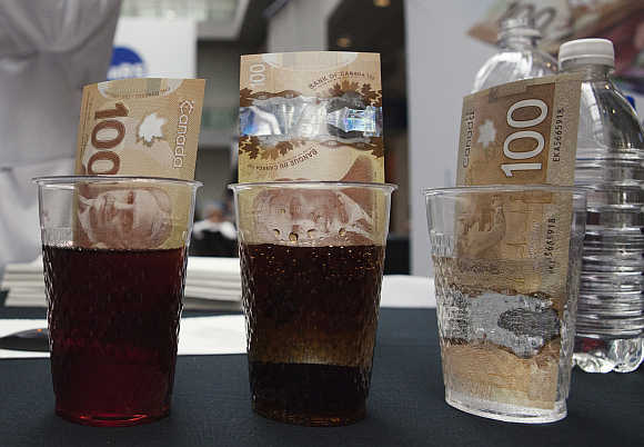 Canadian 100 dollar bills made of polymer are placed in glasses of juice, cola and water in Toronto. Plastic notes, nearly impervious to liquids, stains, tearing or wear-and-tear, were pioneered by the Reserve Bank of Australia in 1988.