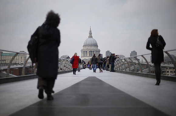 Two women walk along the Millennium footbridge crossing the River Thames towards St Paul's Cathedral in central London, United Kingdom.