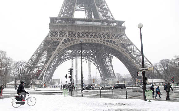 A man rides bicycle as he makes his way along a snow-covered sidewalk near the Eiffel Tower in Paris, France.