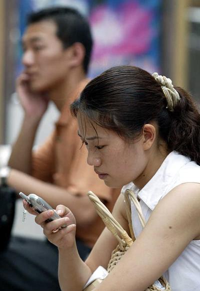 A woman sends text messages while a man chats on his mobile phone in Shanghai, China.