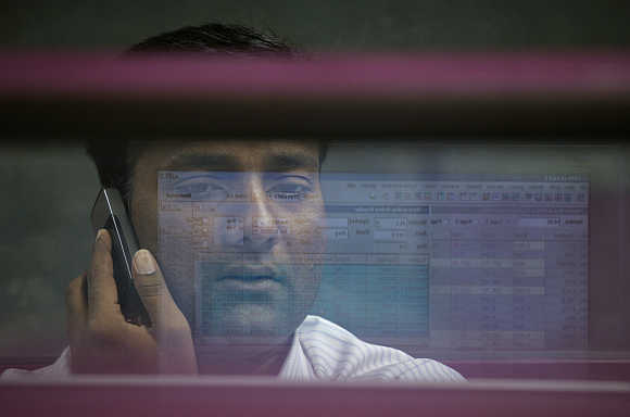 A computer screen is reflected in the glass window of a booth where a broker monitors the market while talking on a mobile phone at the Karachi Stock Exchange in Pakistan.