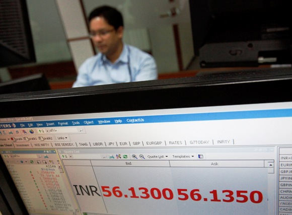 A foreign exchange trader works as the exchange rate of the Indian rupee to U.S. dollar is displayed on a screen at a trading firm in Mumbai.