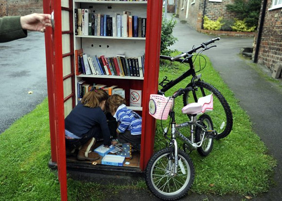 Duncan Berry holds the door open as his children Jemima (L) and Hugo choose books from the village phone box in Marton cum Grafton, northern England.
