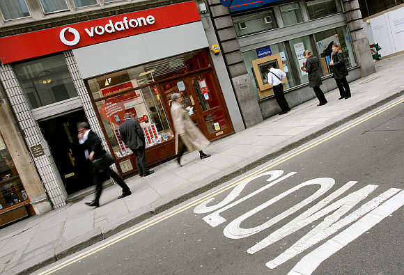Passers-by walk past a Vodafone store in central London.