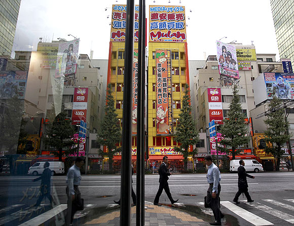 People are reflected on a window as they walk through Tokyo's Akihabara district in Tokyo.