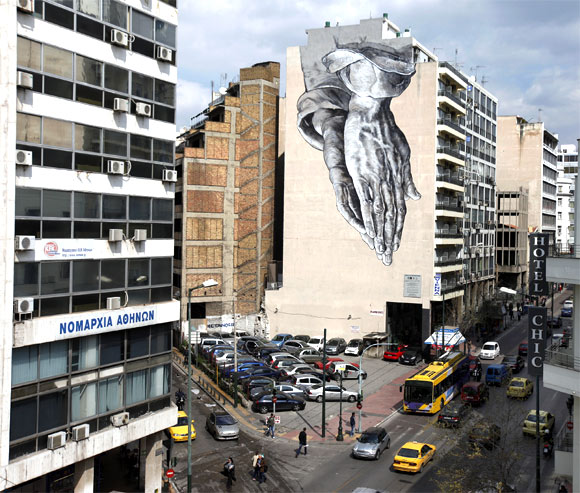 A mural of praying hands is displayed on the side of a hotel in central Athens.