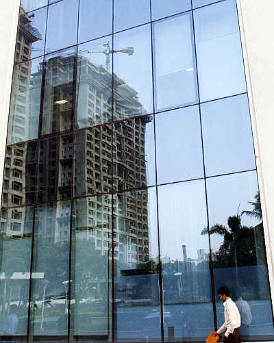 A man walks past a building reflecting the construction of other buildings in Mumbai.