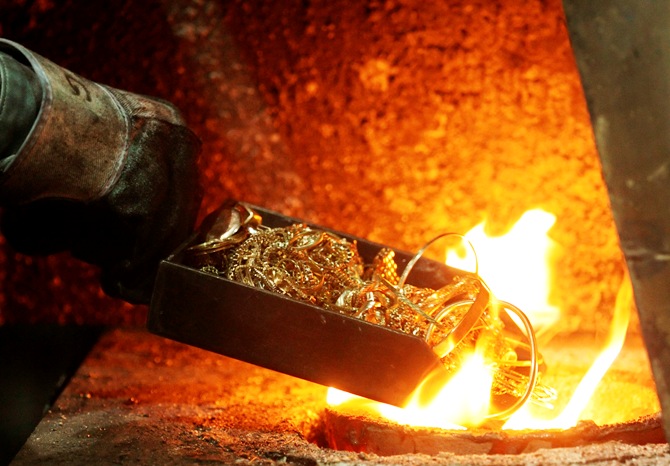 A worker places gold jewellery into a melting furnace.