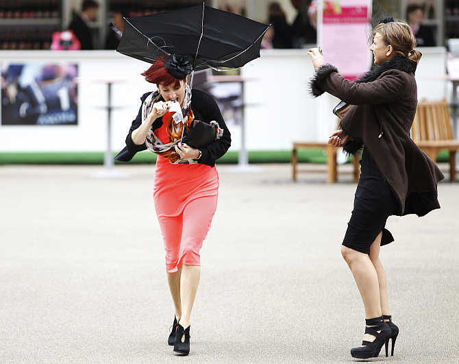 A racegoer struggles with her umbrella in strong winds at Royal Ascot, southwest of London, United Kingdom.