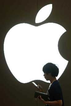 A woman looks at the screen of her mobile phone in front of an Apple logo outside its store in downtown Shanghai, China.