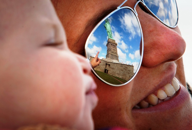 The Statue of Liberty is reflected in the glasses of Katie Ullman as she points to it while she holds her one-year-old son Tyler in her arms on Liberty Island in New York, October 13, 2013.