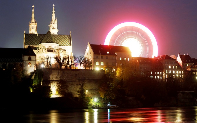 A long time exposure shows a ferris wheel turning beside Basel's landmark the Muenster church on the borders of the Rhine river.
