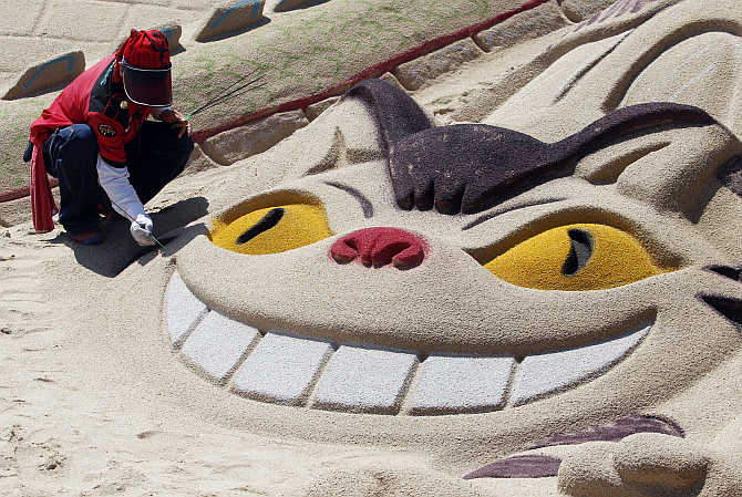 An artist adds finishing touches to a sand sculpture of a cat at the Haeundae Sand Festival in Busan, South Korea.