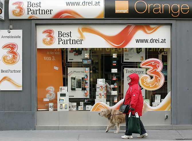 A woman and her dog walk by a telecommunications store advertising Orange in Vienna, Austria.