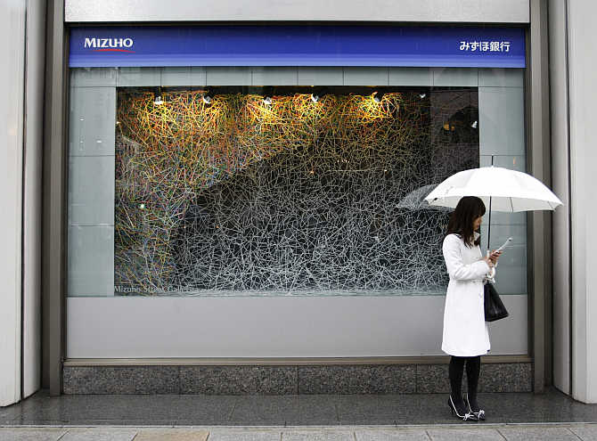 A woman stands under an umbrella outside a Mizuho bank branch in Tokyo.