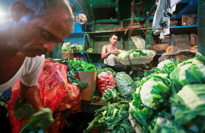 A vendor weighs vegetables as another sorts them at their stall at a wholesale food market in Mumbai.