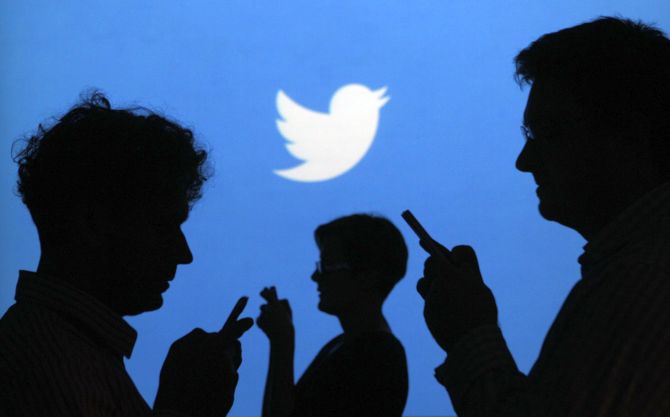 People holding mobile phones are silhouetted against a backdrop projected with the Twitter logo.