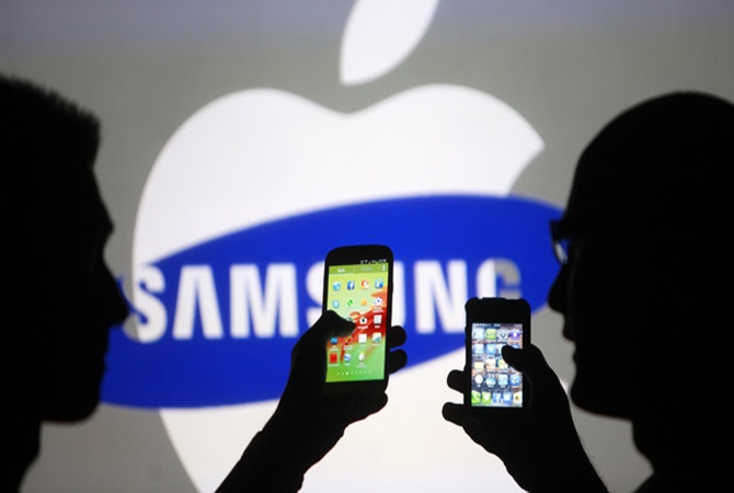 Men are silhouetted against a video screen with an Apple Inc logo as they pose with a Samsung Galaxy S3 smartphone in this photo illustration.