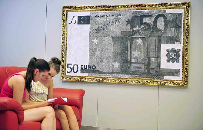 Women look through a catalogue near a painting of a euro banknote during an exhibition by designer Alexsander Brezlan at the Faculty of Economics at the University of Ljubljana, Slovenia.