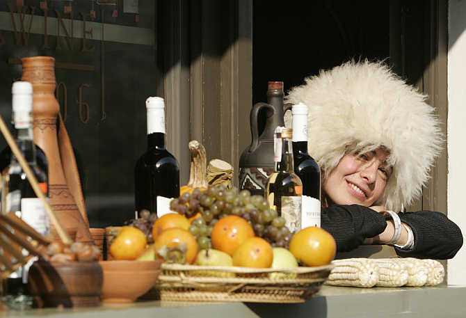 A shop assistant wearing a Georgian traditional hat smiles as she sells wine and fruit during the Tbilisoba city day celebration in Tbilisi, Georgia.