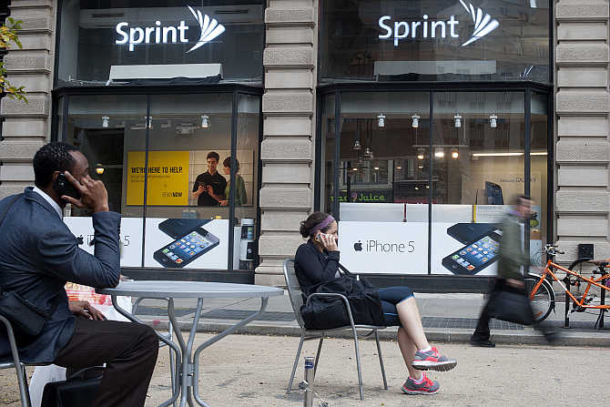 People talk on their mobile phones as passers-by walk past a Sprint store in New York.