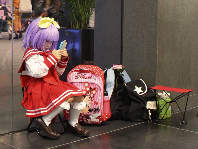A young cosplayer plays with her mobile phone as she rests after attending the Anime Festival Asia in Singapore.